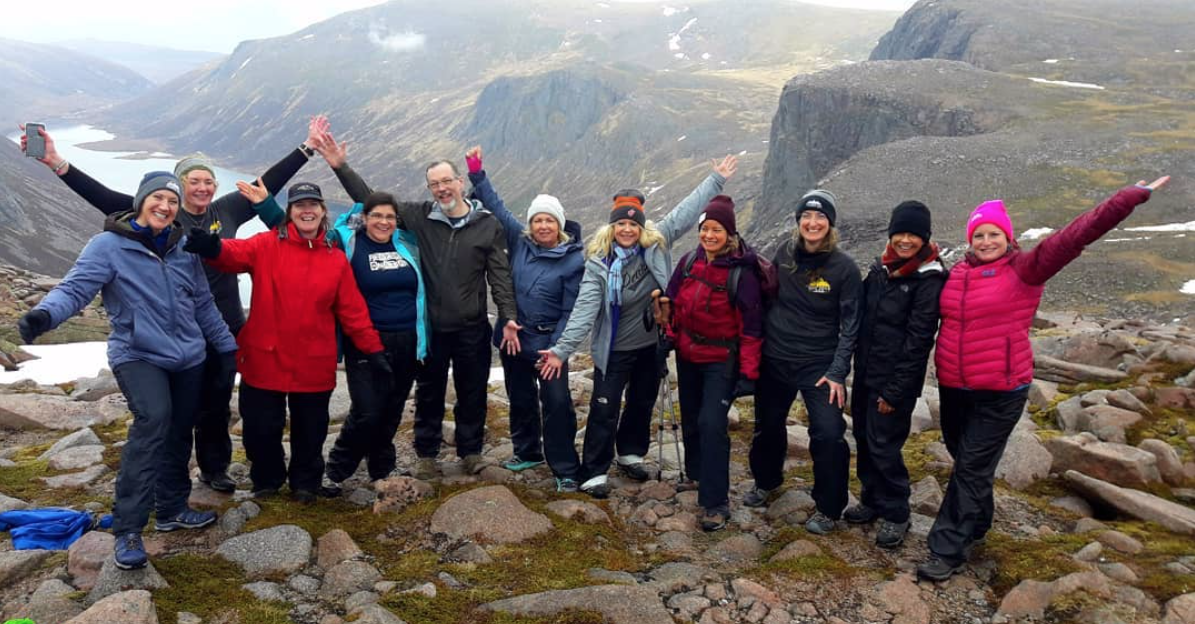 A smiling corporate group pose for a photo above Loch Avon in the Cairngorms after summiting Ben Macdui
